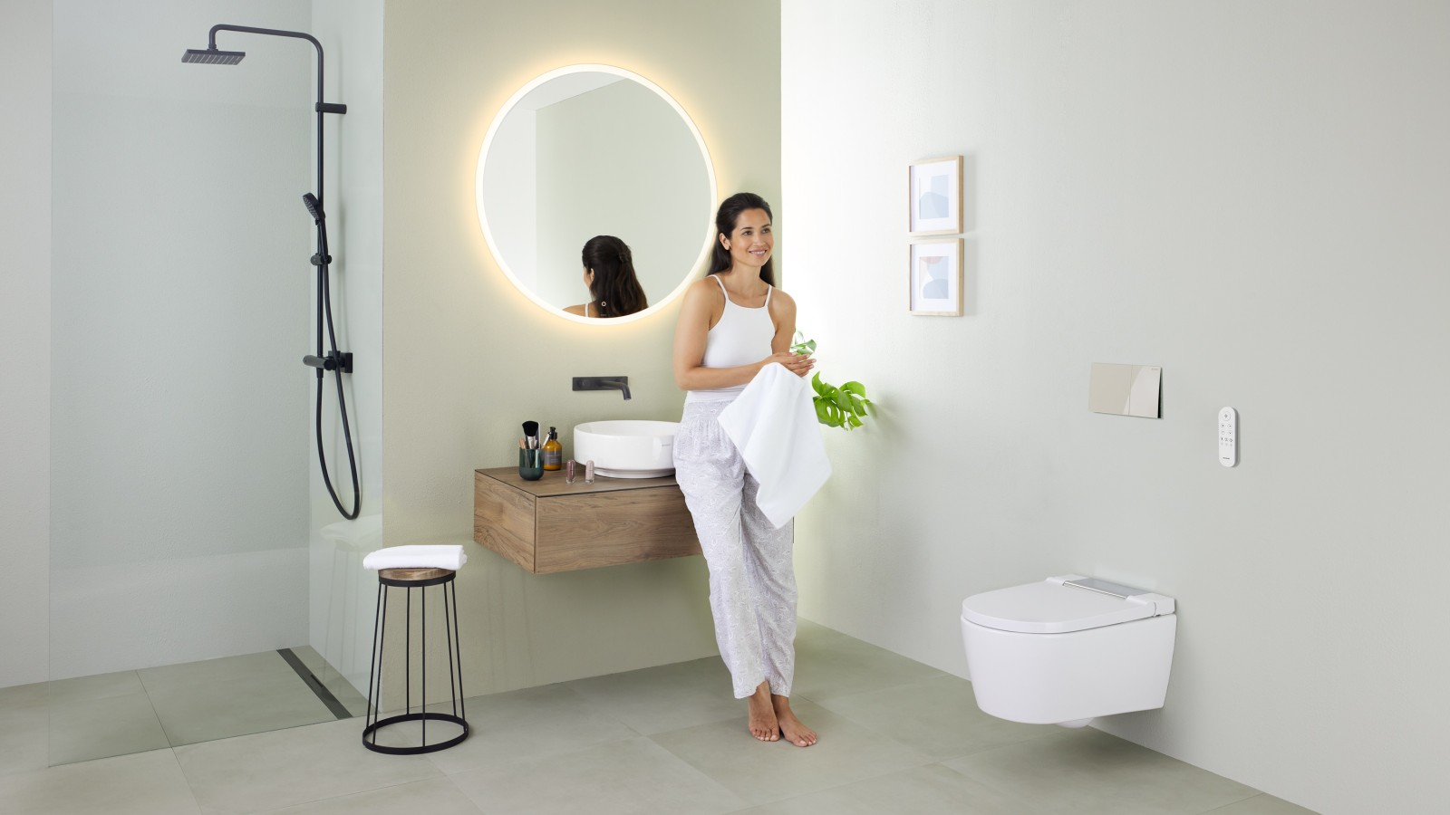 Geberit AquaClean Sela dušš-WC ja Geberit VariForm valamu ning mööbliga vannitoas valamule nõjatuv naine Geberit AquaClean Sela dušš-WC ja Geberit VariForm valamu ning mööbliga vannitoas valamule nõjatuv naine